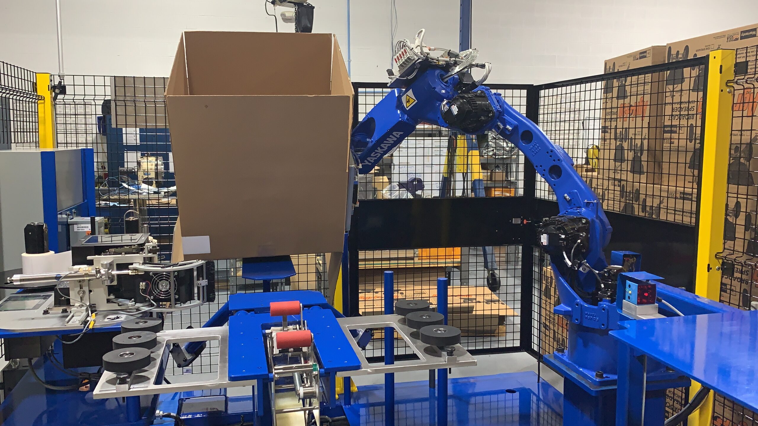 Robotic case erector in operation, lifting a cardboard box, part of automated material handling and packaging system by Versatech.