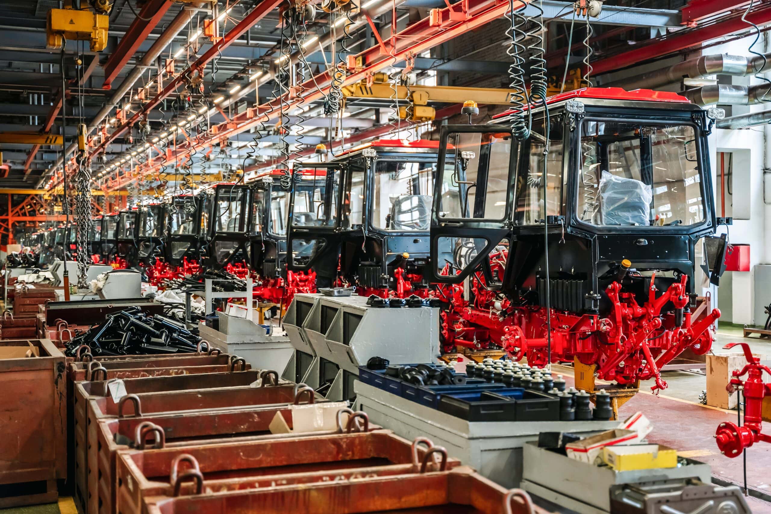 Heavy machinery assembly line with tractor cabs and red chassis components, showcasing industrial automation in agriculture and heavy industries.