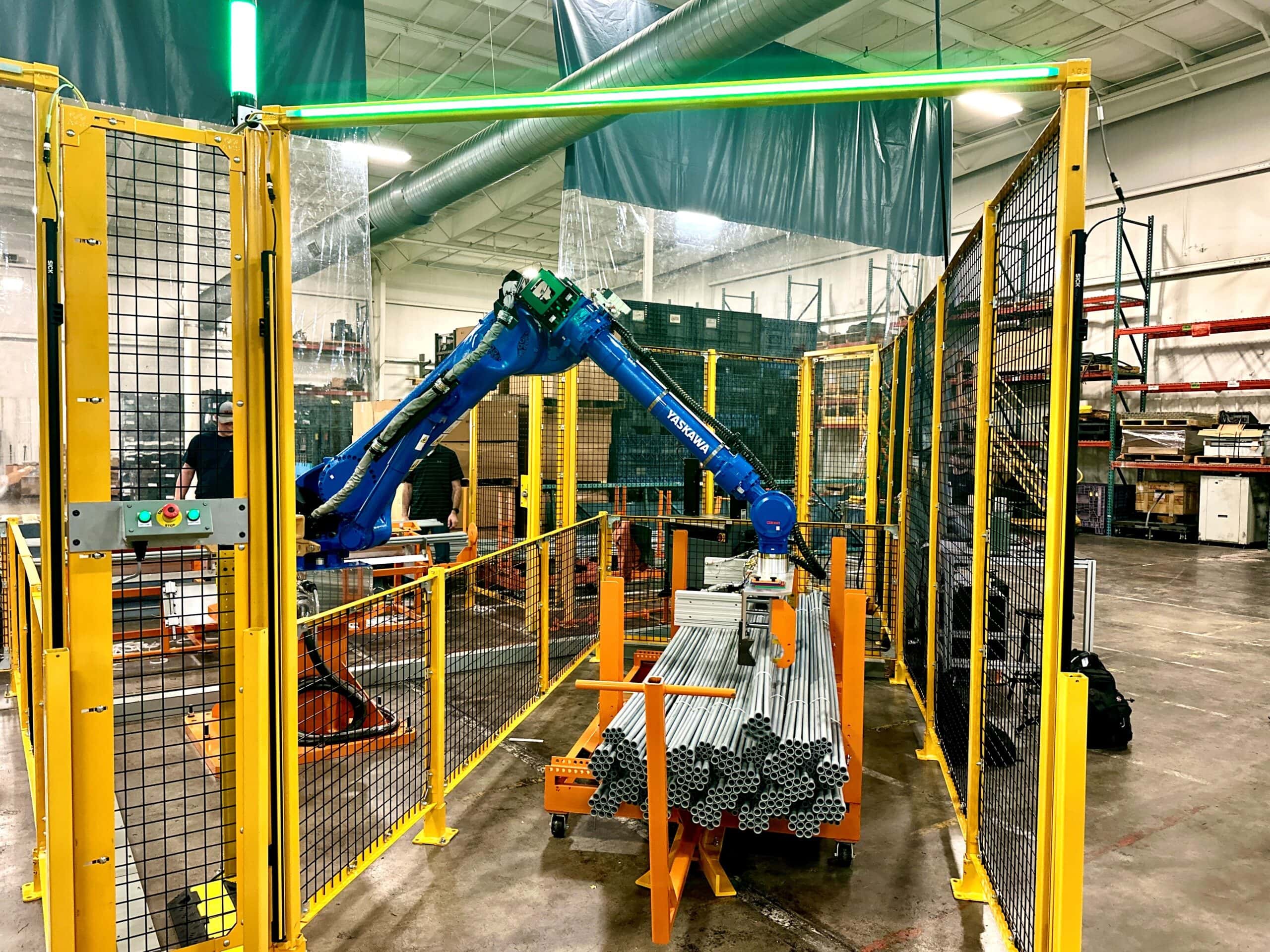 Robotic arm in automated material handling system, efficiently managing pipes in a secured workspace with safety fencing and control panel.