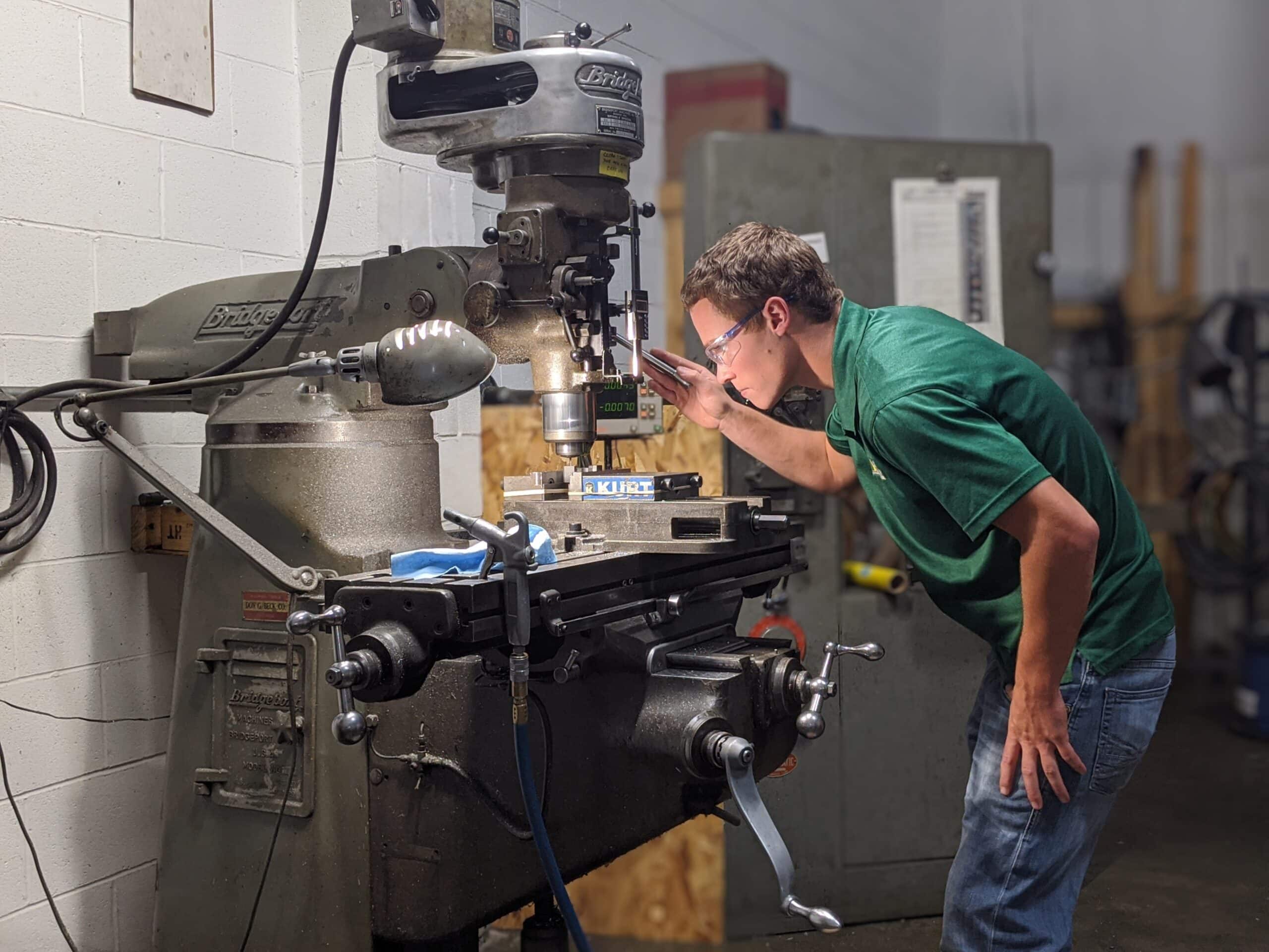 Machinist Man operating a Bridgeport milling machine in a workshop, focusing on precision machining for custom automation solutions.